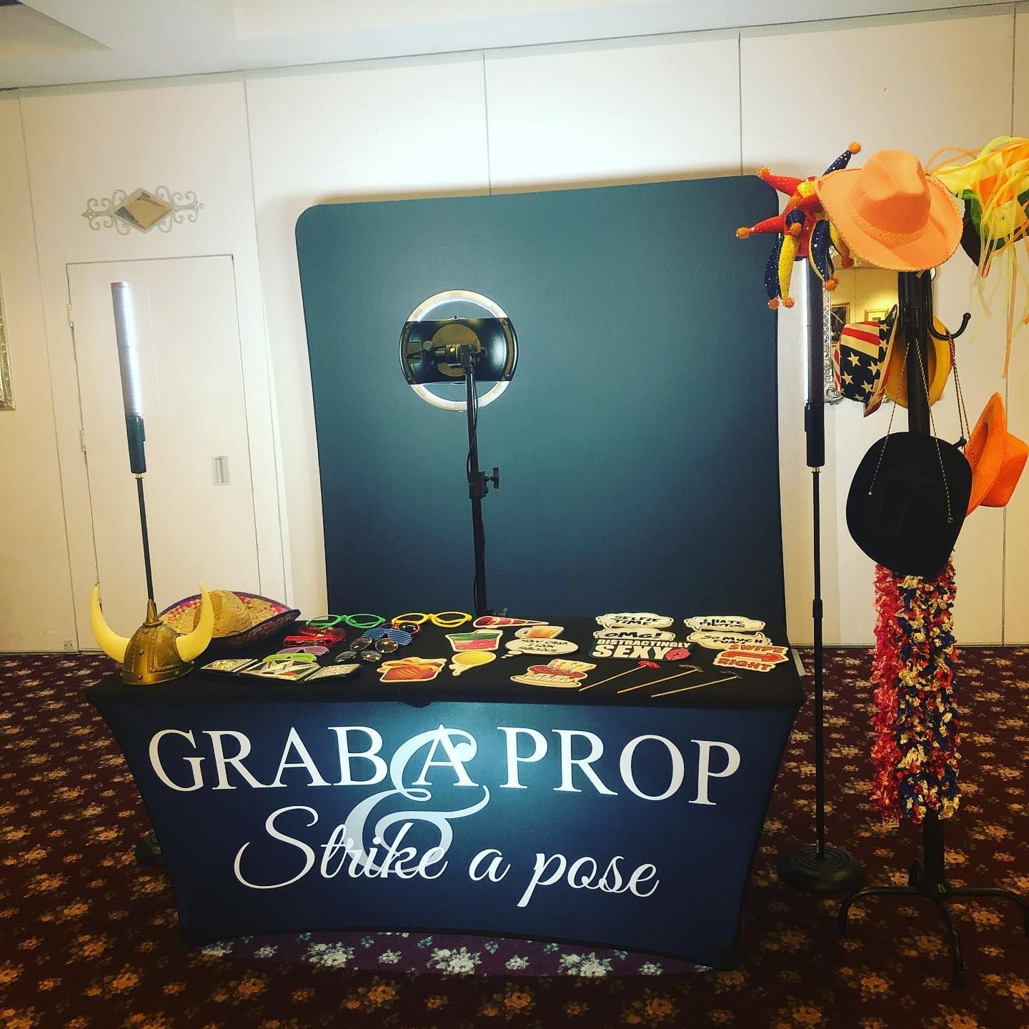 Photo booth setup with props: backdrop, camera, props table, and hat rack.