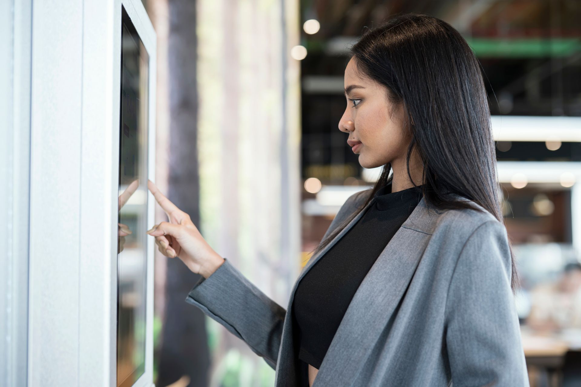 Woman in gray blazer interacts with a touchscreen display, indoors.