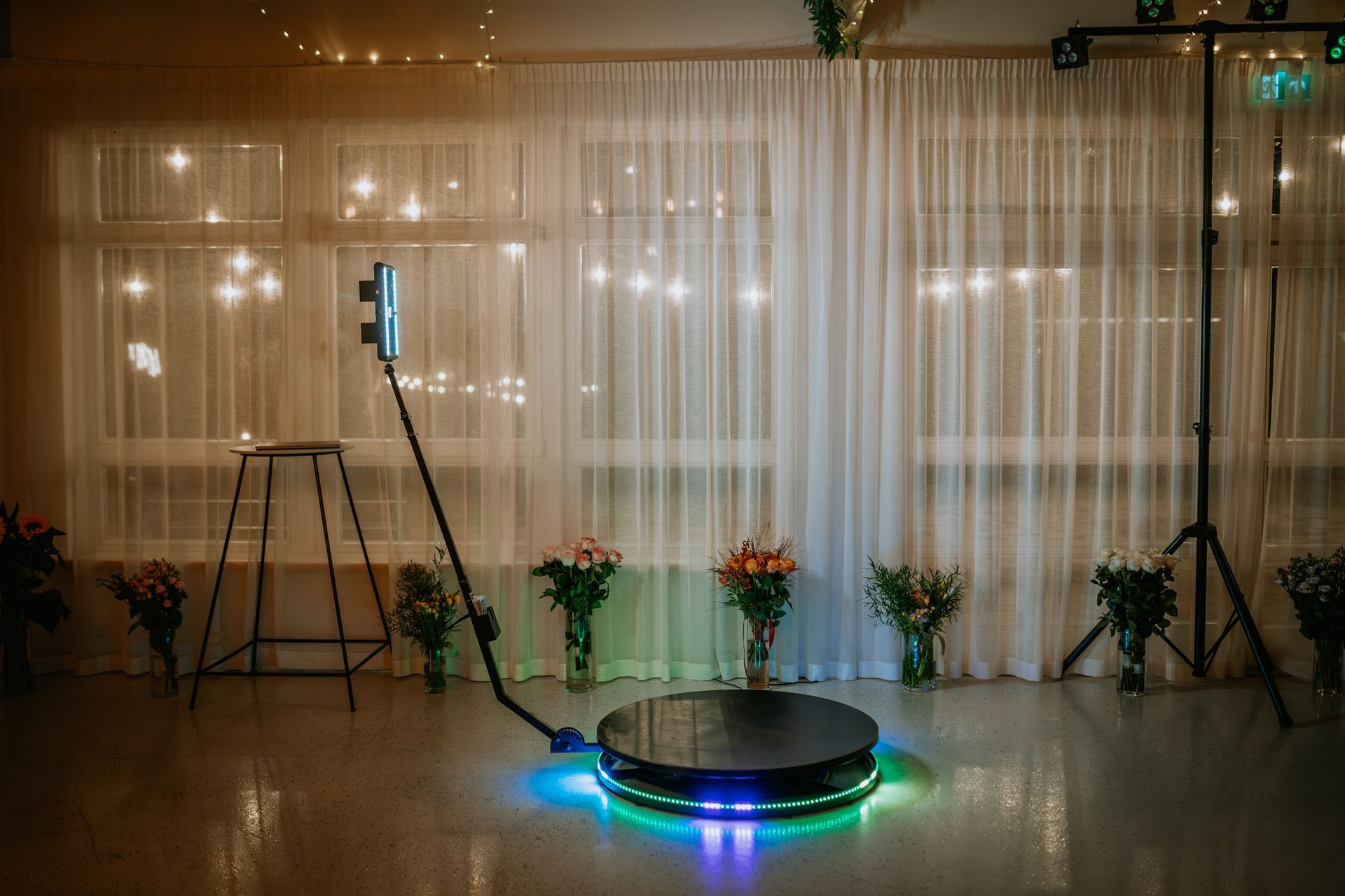360 photo booth setup with flowers, lights, and a white curtain backdrop.