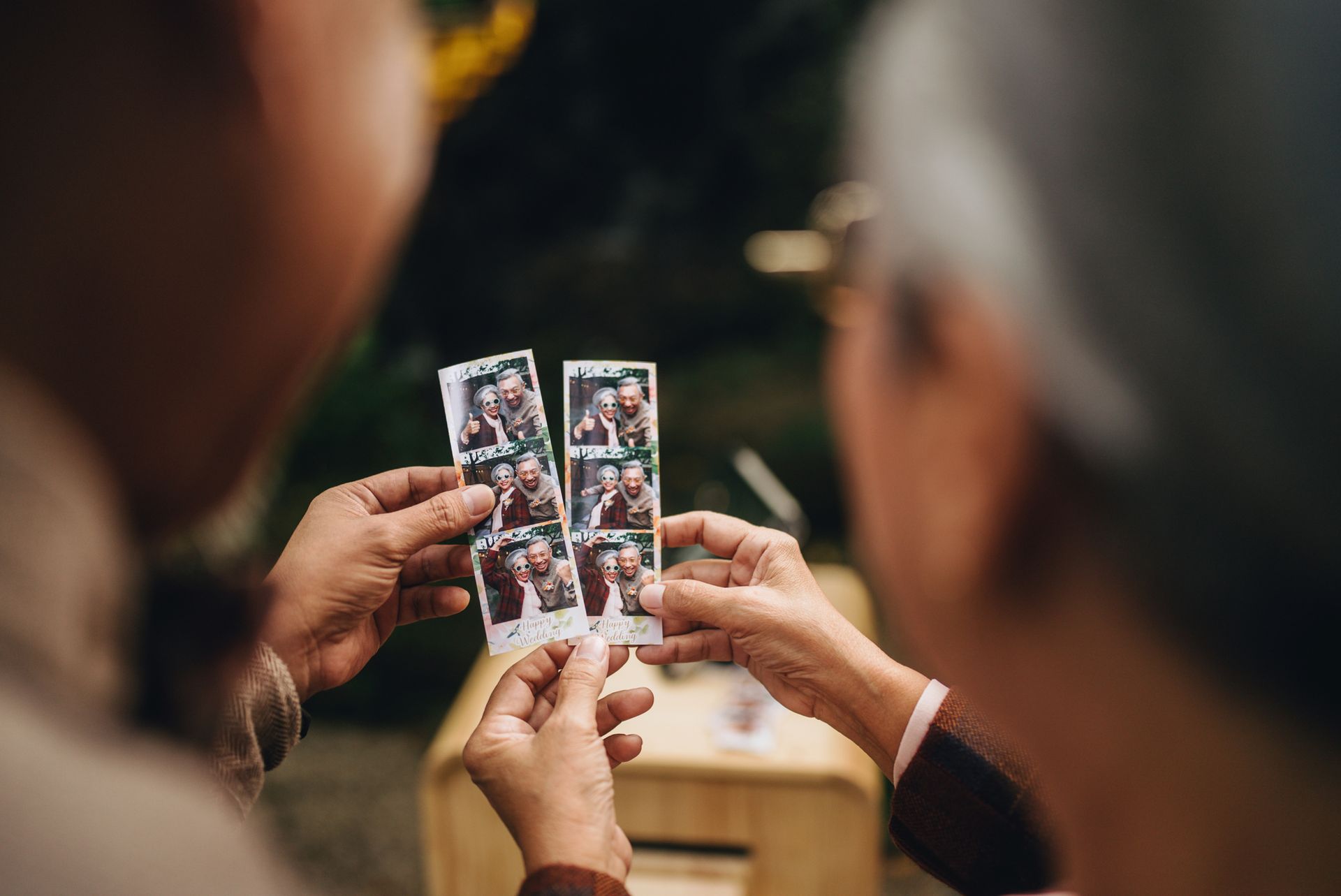Two people looking at photo booth strips outdoors.