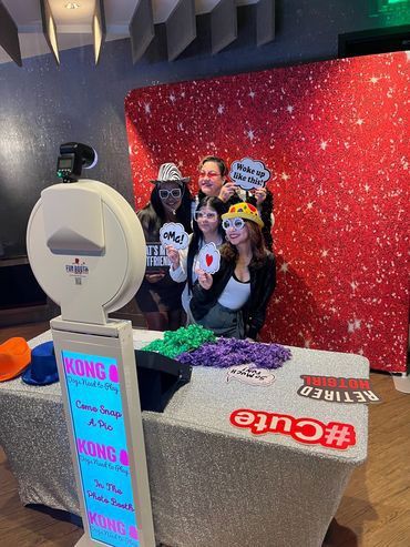 People posing at a photo booth with props, in front of a sparkly red backdrop.