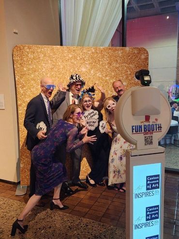 Group of people posing with props at a photo booth with gold backdrop; fun expressions.