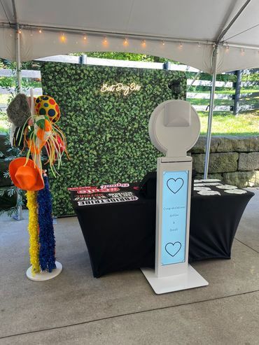 Photo booth with props in front of a greenery backdrop under a white tent.