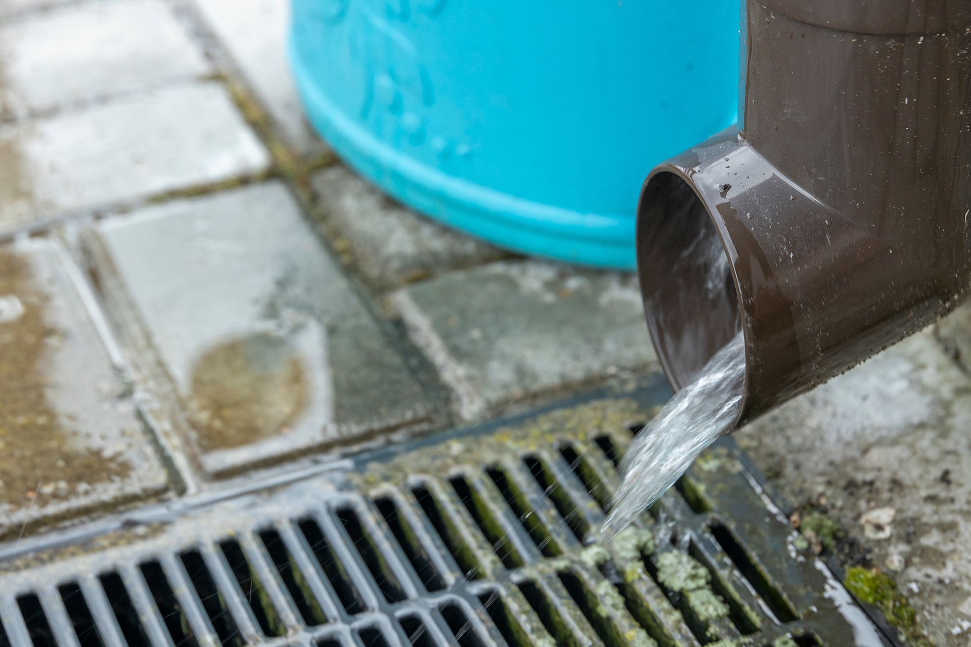 A brown pipe is pouring water into a drain.