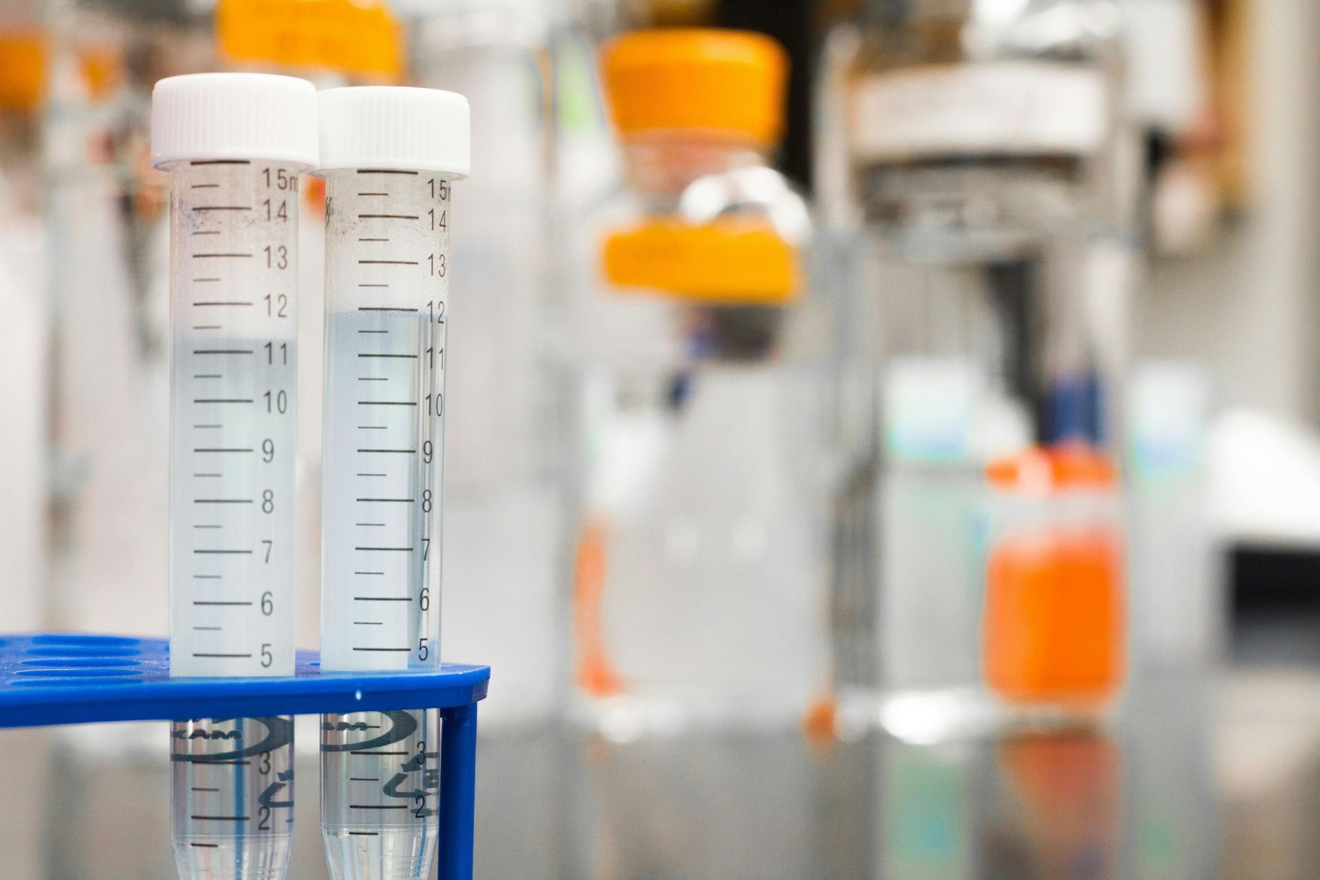 Two filled test tubes in a blue rack, blurred lab equipment in the background.