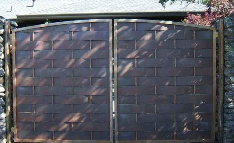 Two brown metal gates with a woven brick pattern, set between stone walls.