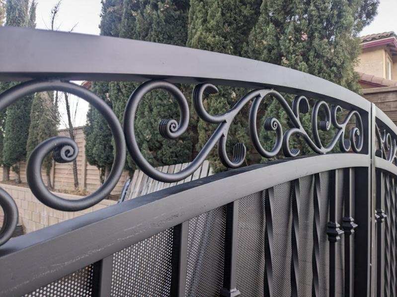 Black wrought iron gate with scrollwork details, arched top, and vertical bars and Ornamental iron work on it.