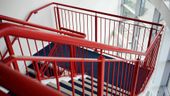 Red metal staircase with blue and white striped steps, descending in a building.