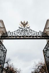 Ornate black iron gate with golden emblem, open to overcast sky. 