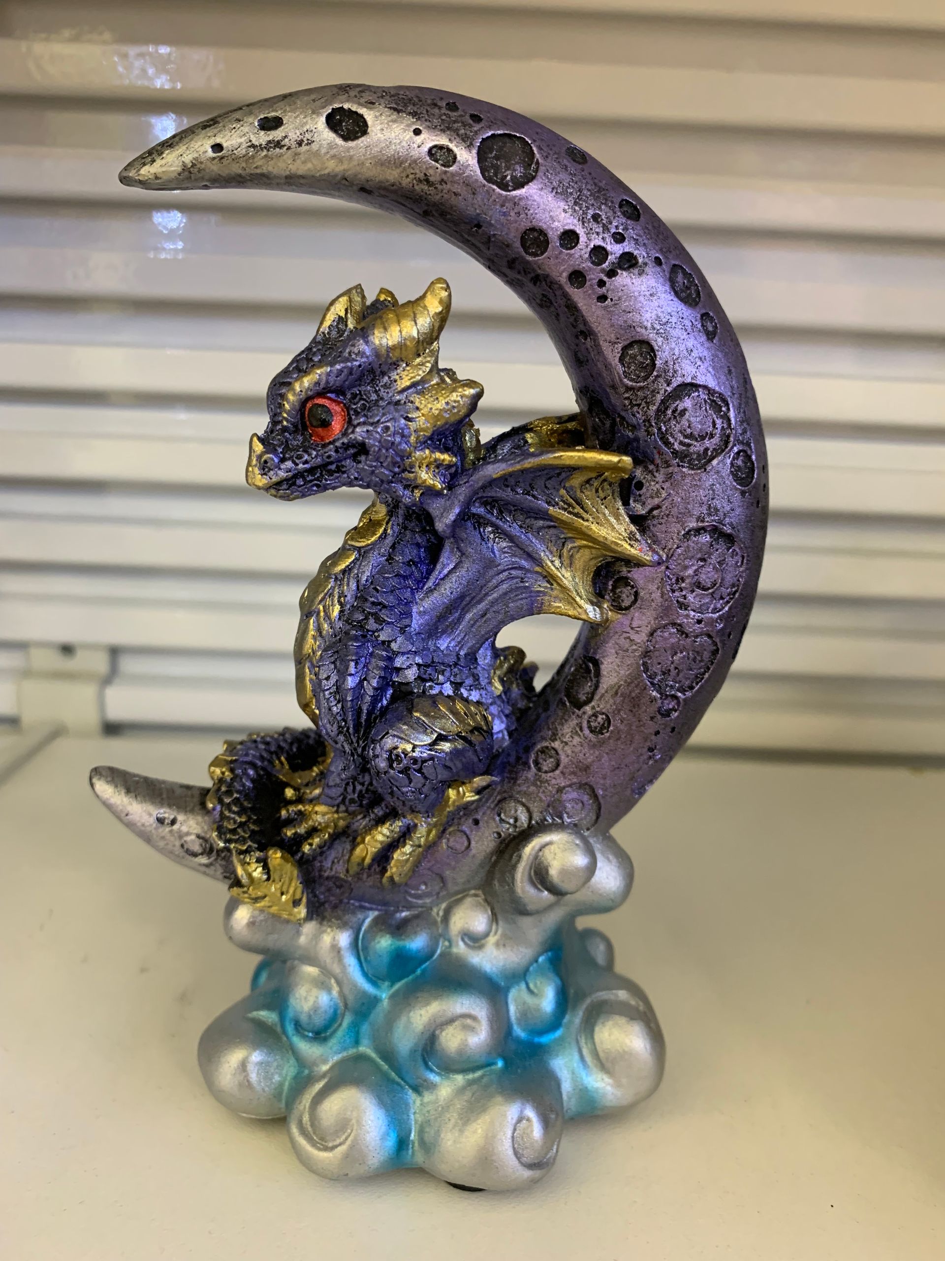 A purple and gold dragon is sitting on a purple crescent moon.