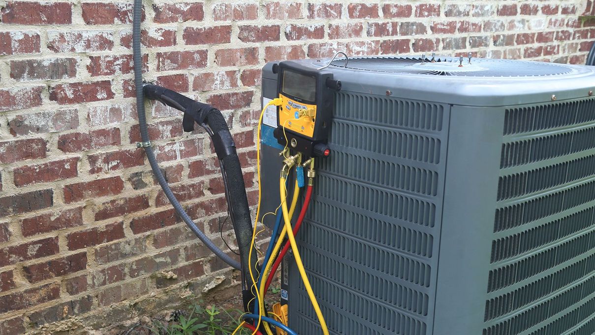 An air conditioner is being serviced in front of a brick wall.