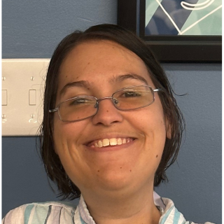 Woman with glasses smiling at camera; blue wall background.