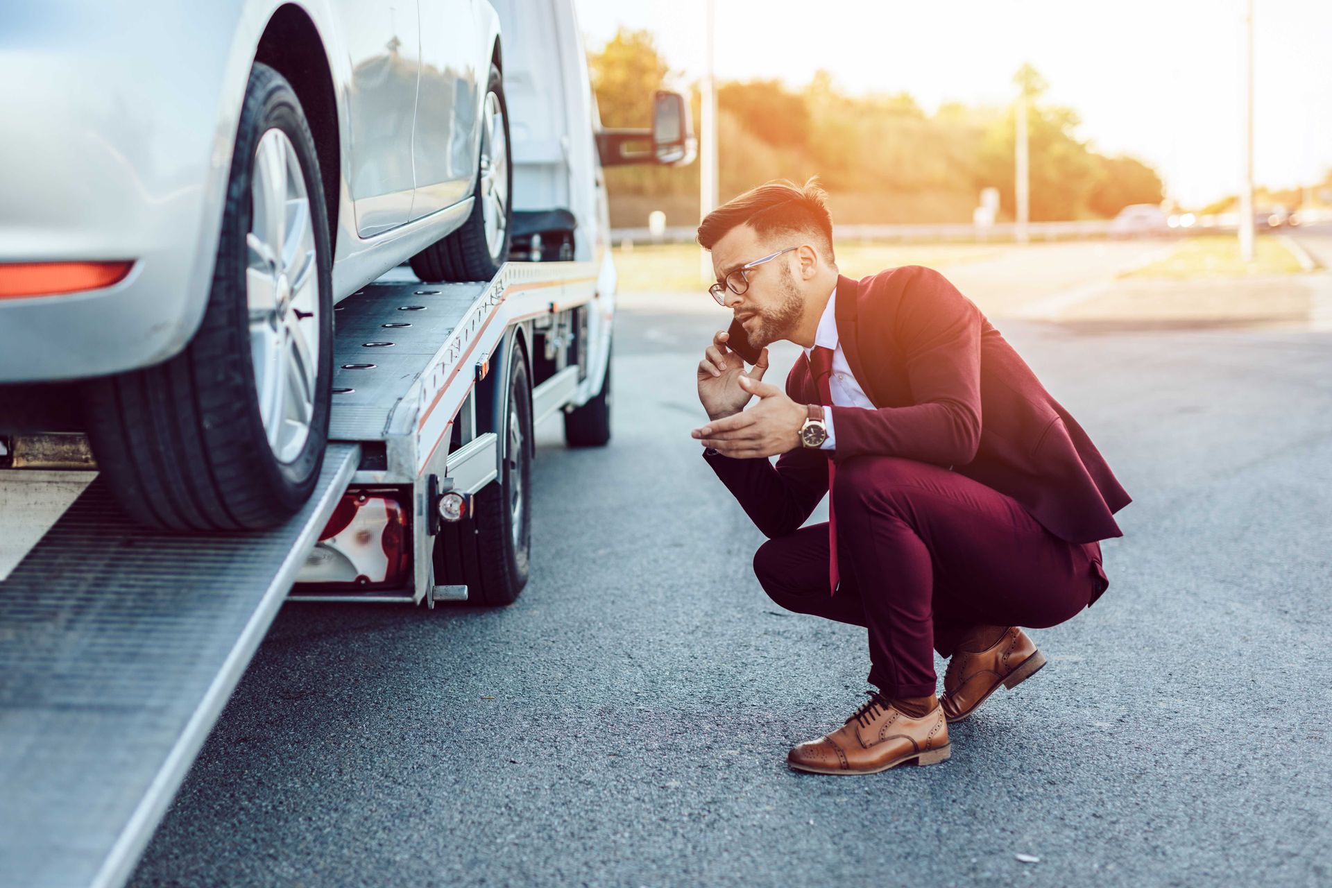 a man in a suit is kneeling down next to a tow truck with a car on it