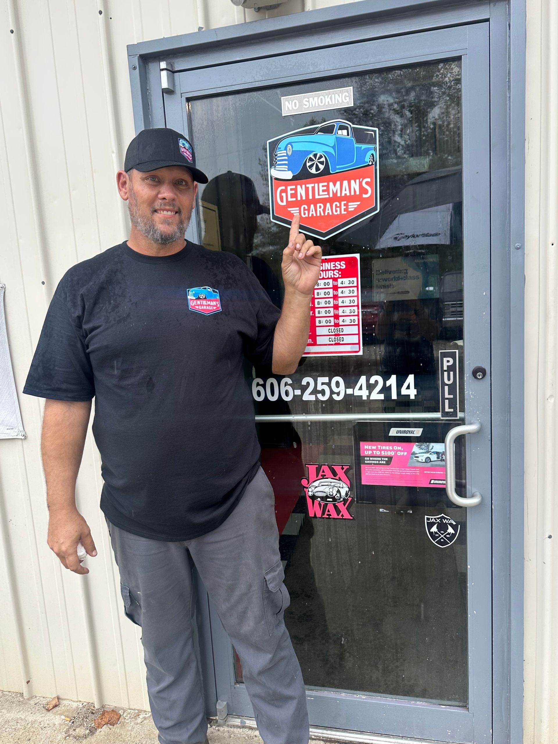 Man standing in front of Gentlemen's Auto Detail door, pointing up; phone number 606-259-4214 visible. | Gentleman’s Garage