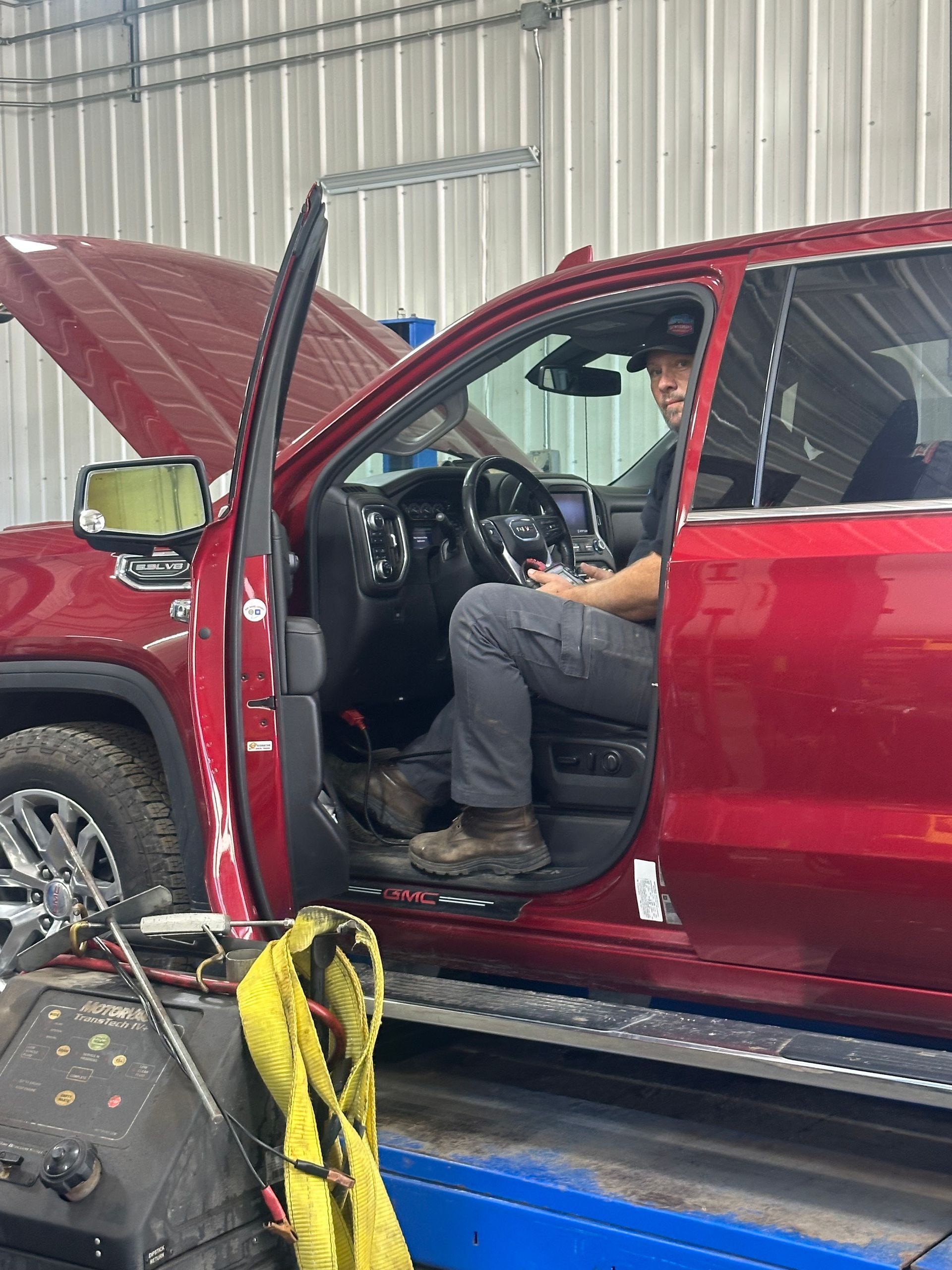 Mechanic in red truck with open hood; inside, using a device. Shop setting. | Gentleman’s Garage