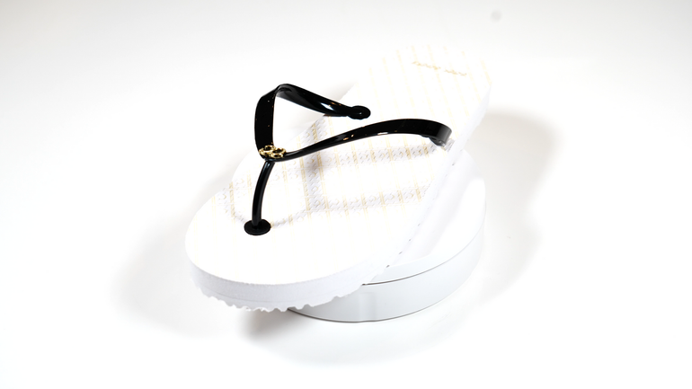 A pair of white flip flops with black straps on a white surface.