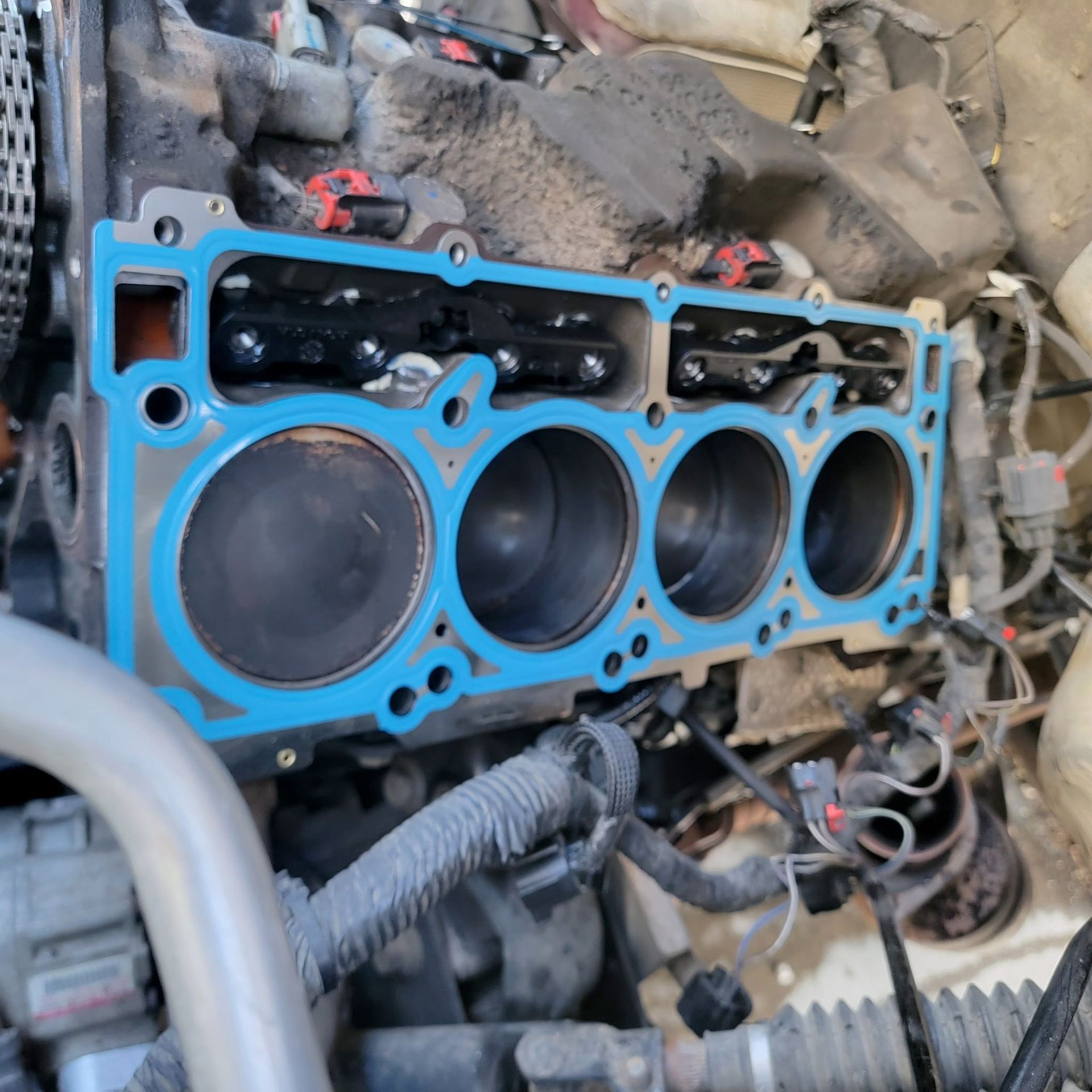 A bright blue engine head gasket seated on a car engine block with four visible cylinders.
