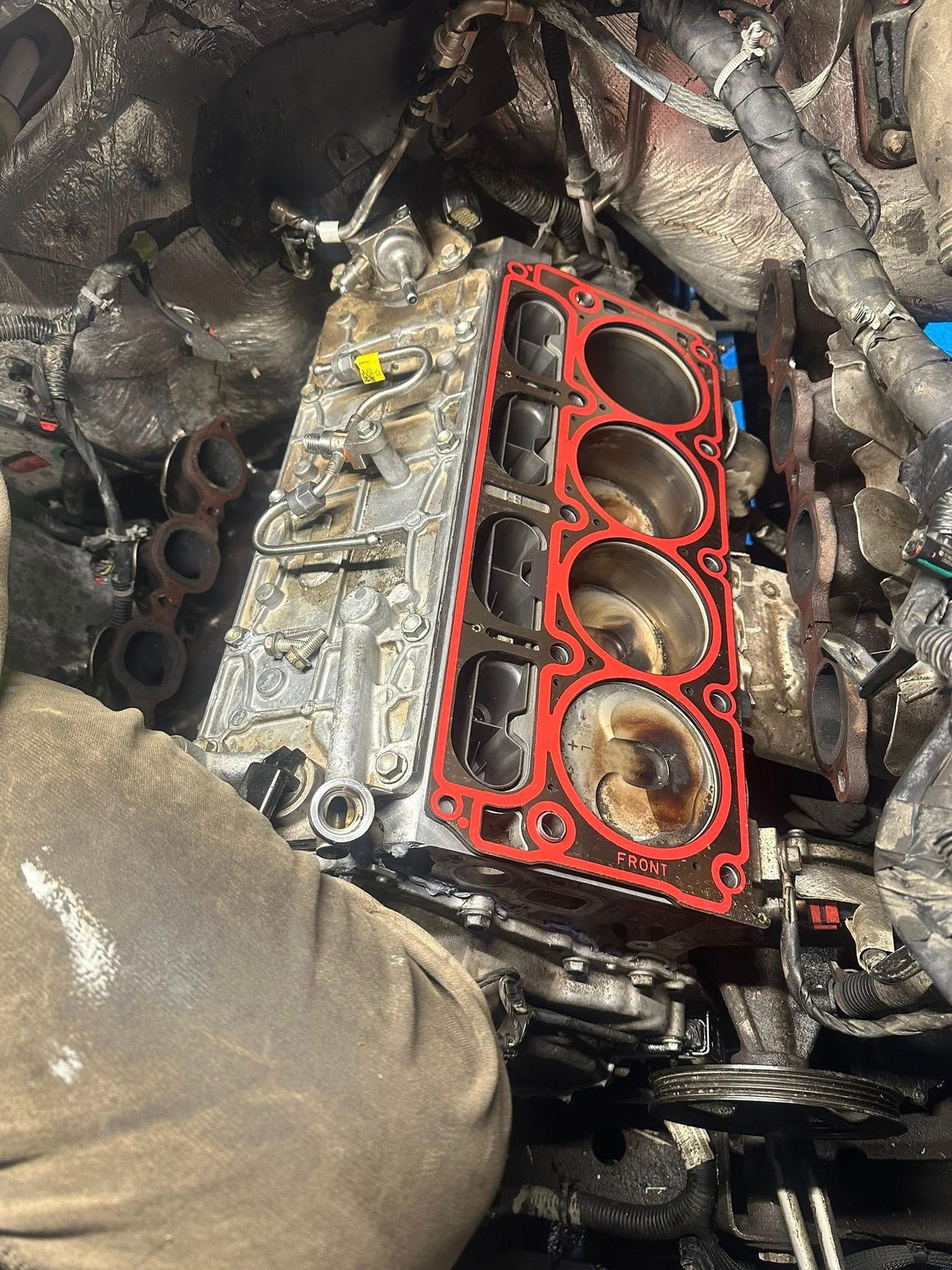 An engine block with pistons visible, featuring a bright red head gasket positioned on the metal surface.