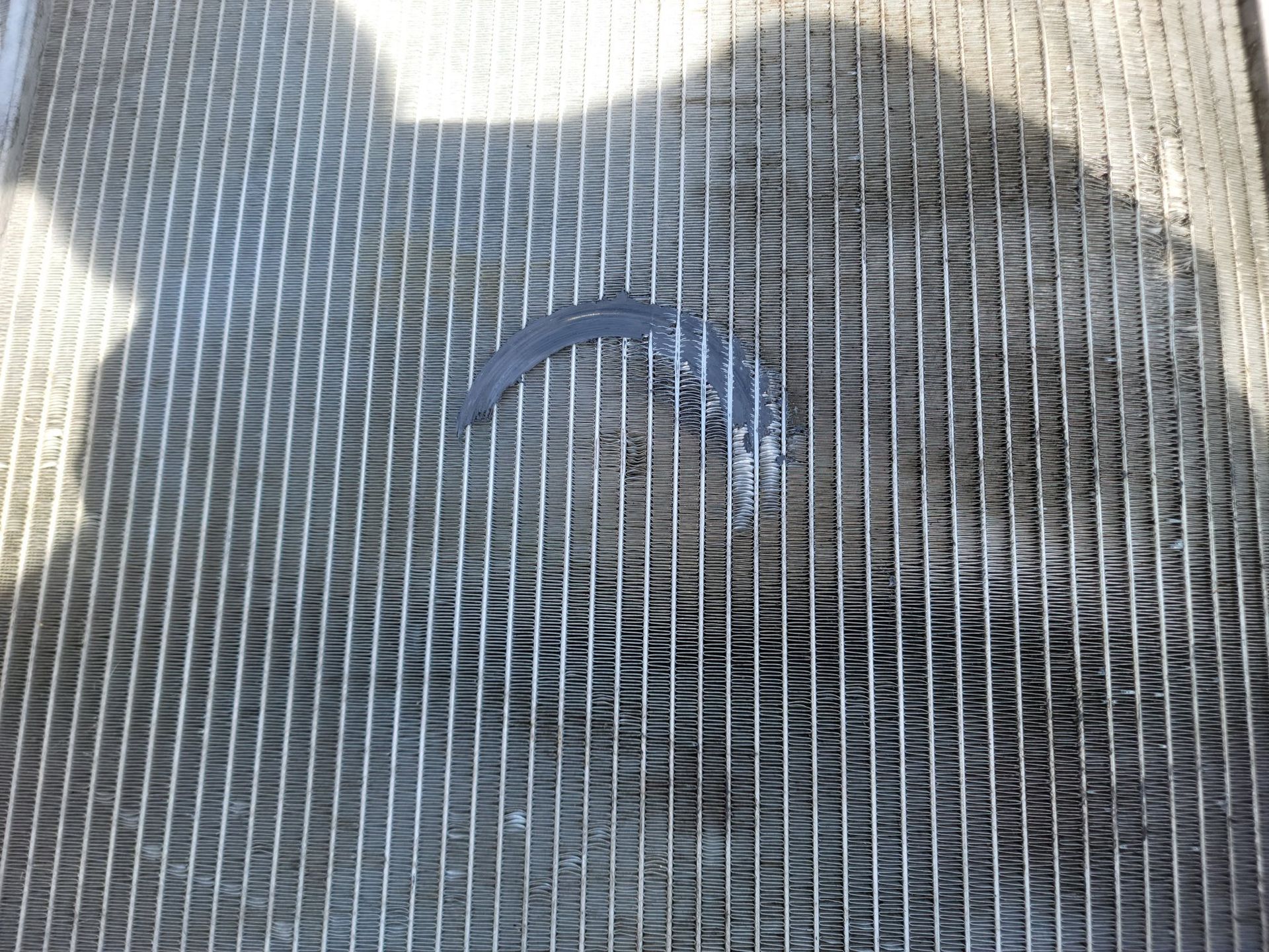 A close-up view of a metal radiator grill with a dark, curved crescent-shaped obstruction embedded in the center.