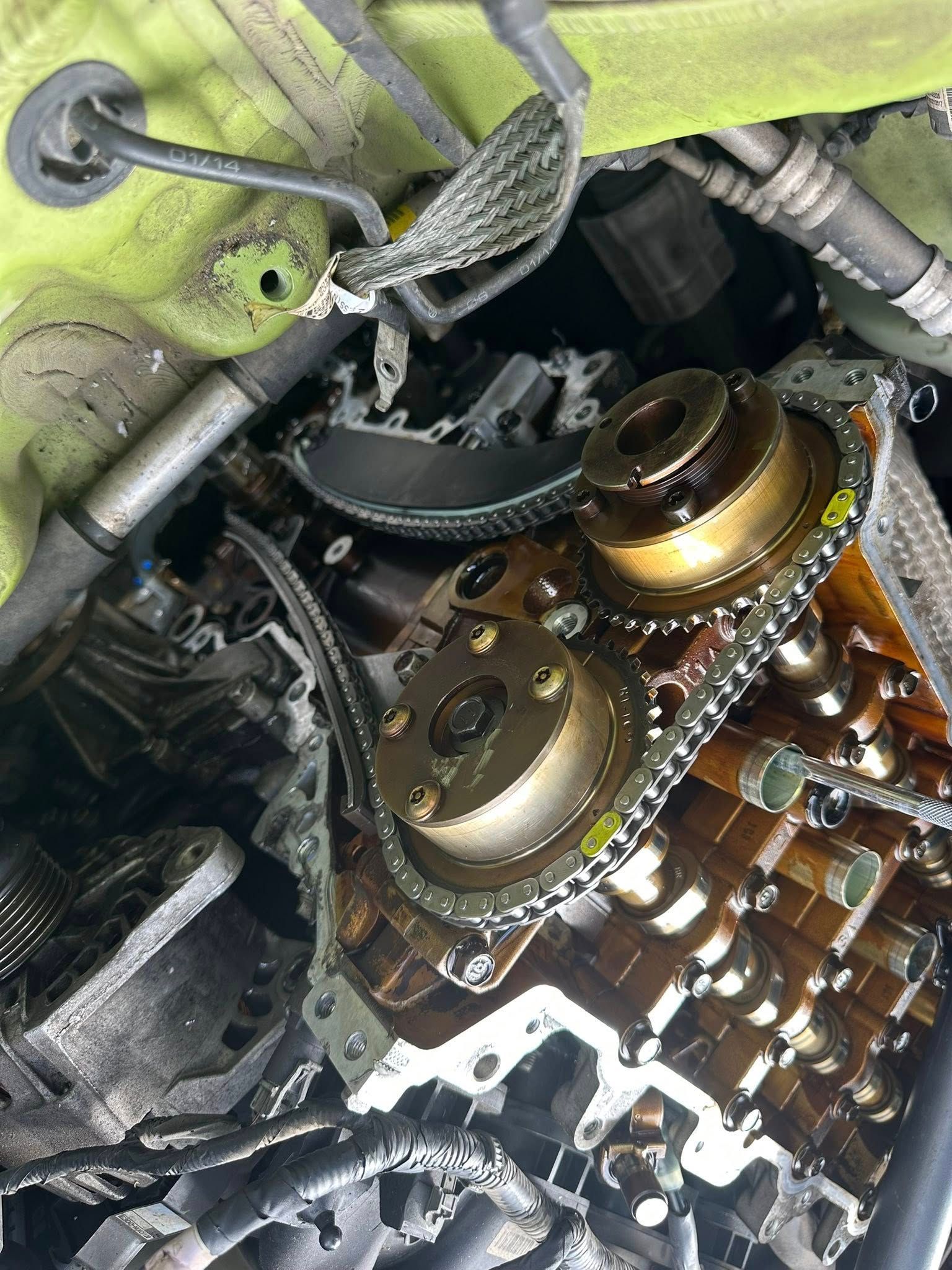 An open car engine showing camshaft sprockets, a timing chain, and internal components lubricated with dark engine oil.