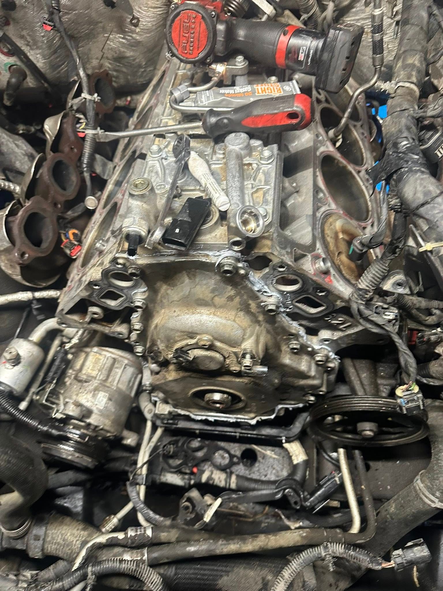 A close-up view of an exposed, dirty car engine block with various mechanical components and tools resting on top.