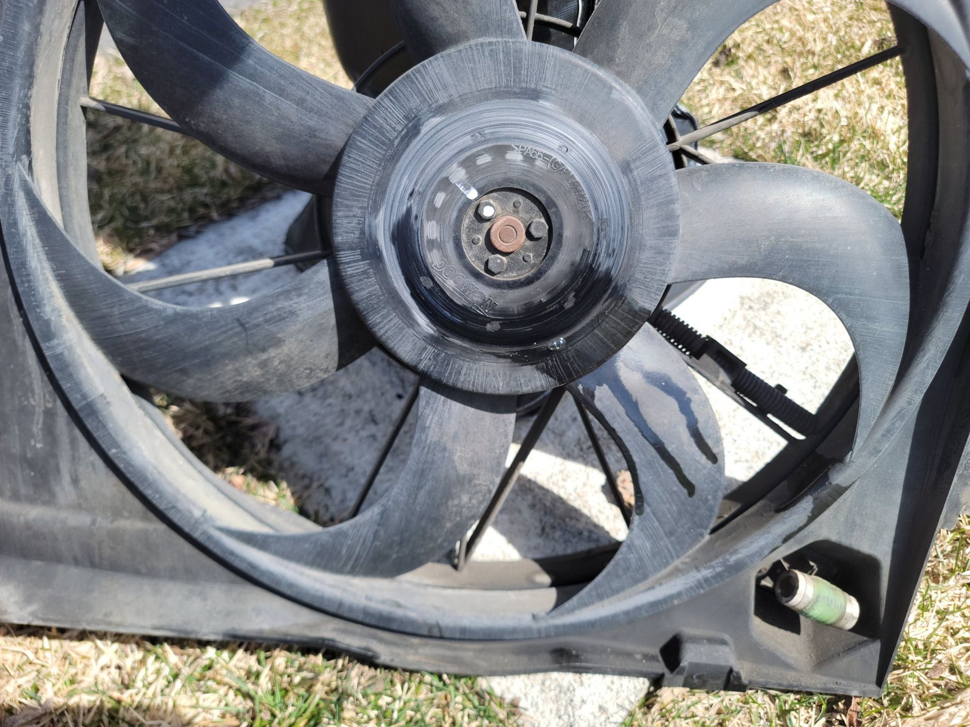 A black automotive radiator cooling fan assembly resting on a patch of grass.
