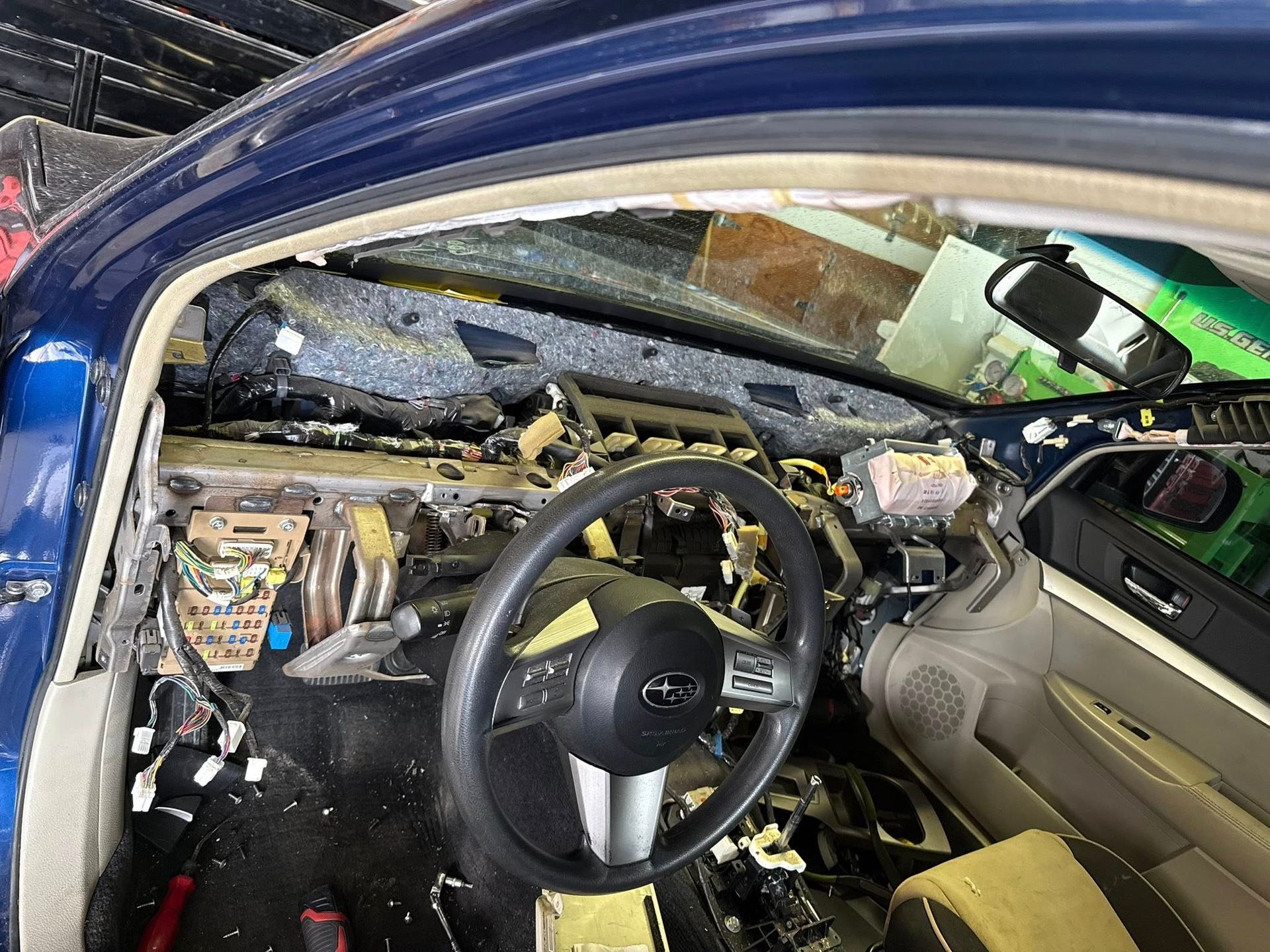 Interior of a blue car with the dashboard removed, exposing the steering wheel, wiring, and metal frame.