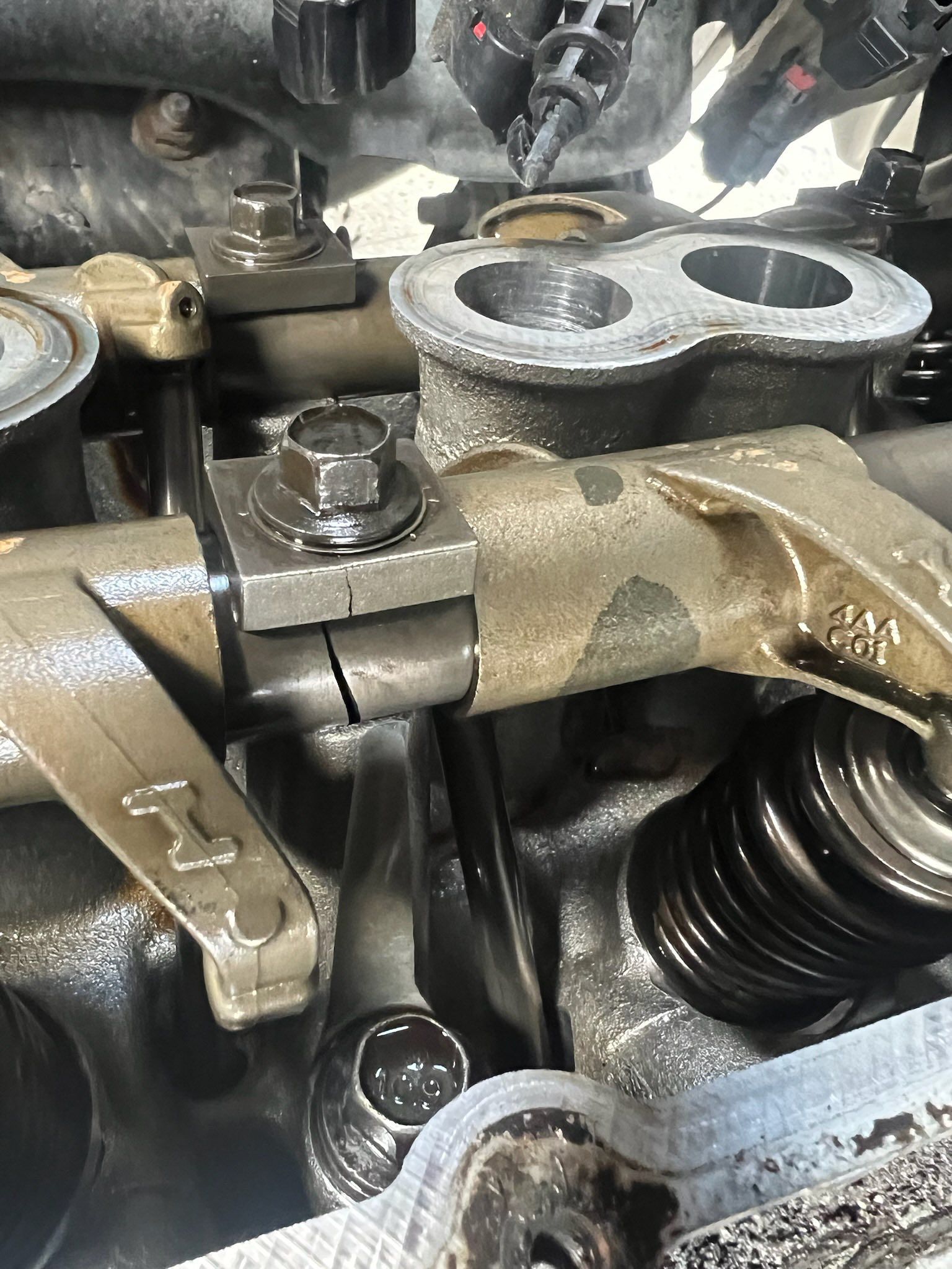 A cracked rocker arm assembly inside a vehicle engine cylinder head.