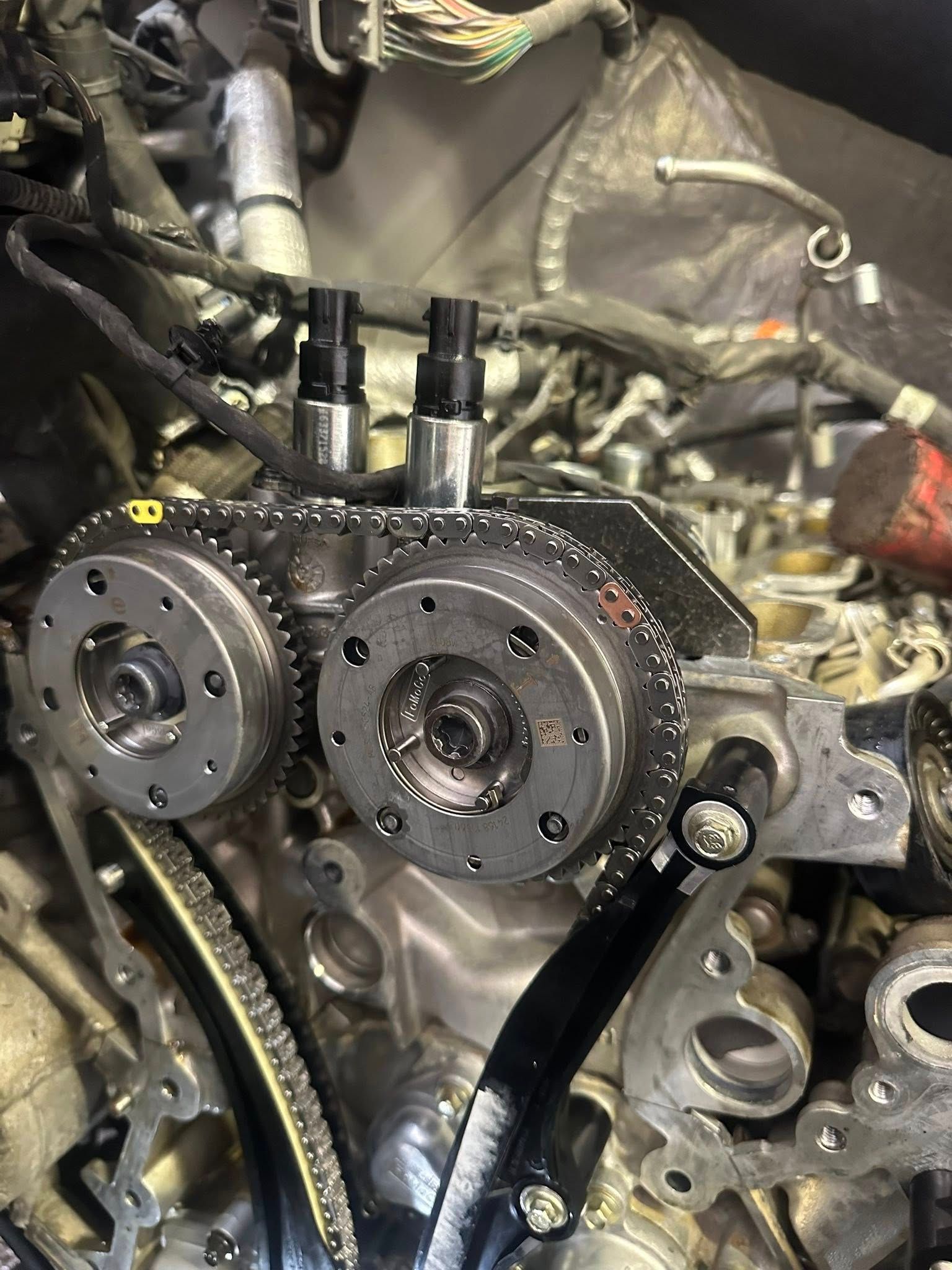 The front view of a car engine with timing chains, sprockets, and two VVT solenoids installed.