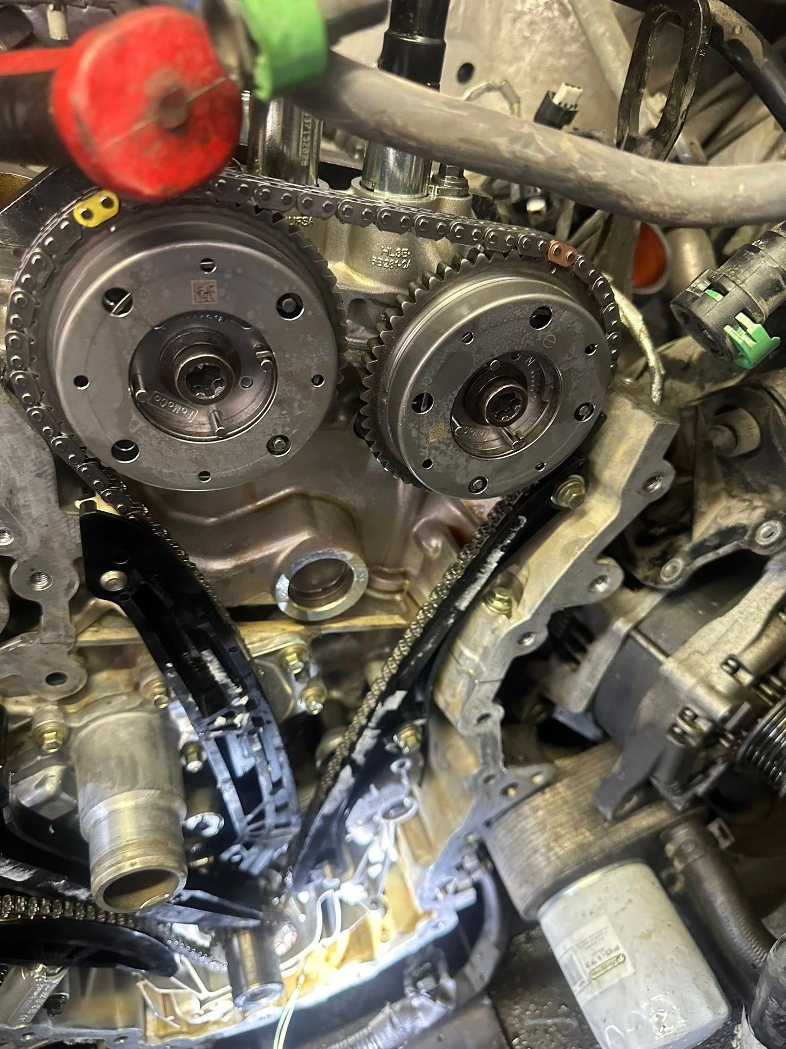 Engine block of an automobile, showing the timing chain assembly and two metal cam phasers mounted to the engine.