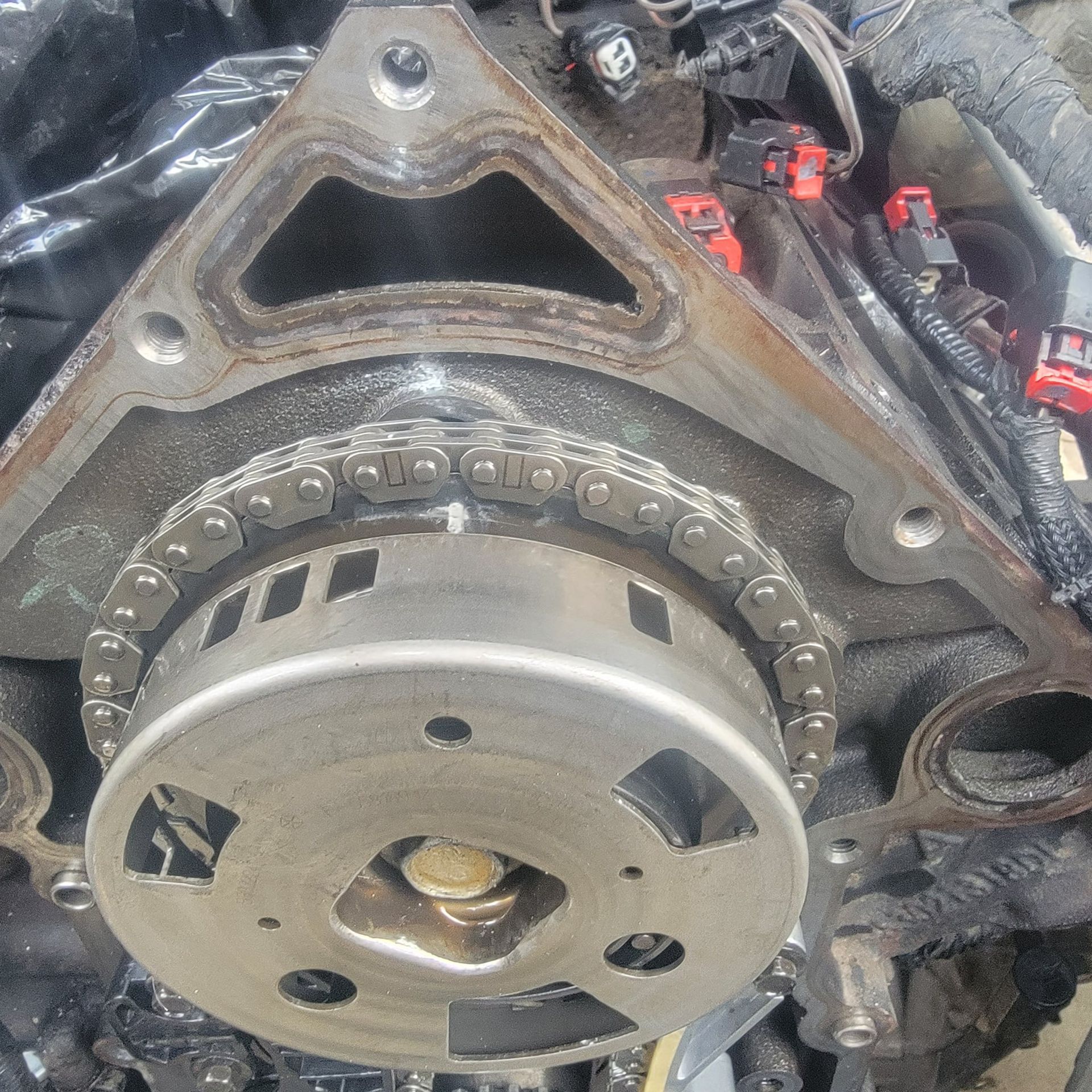 Close-up of a vehicle engine timing chain and cam phaser assembly exposed during repair.