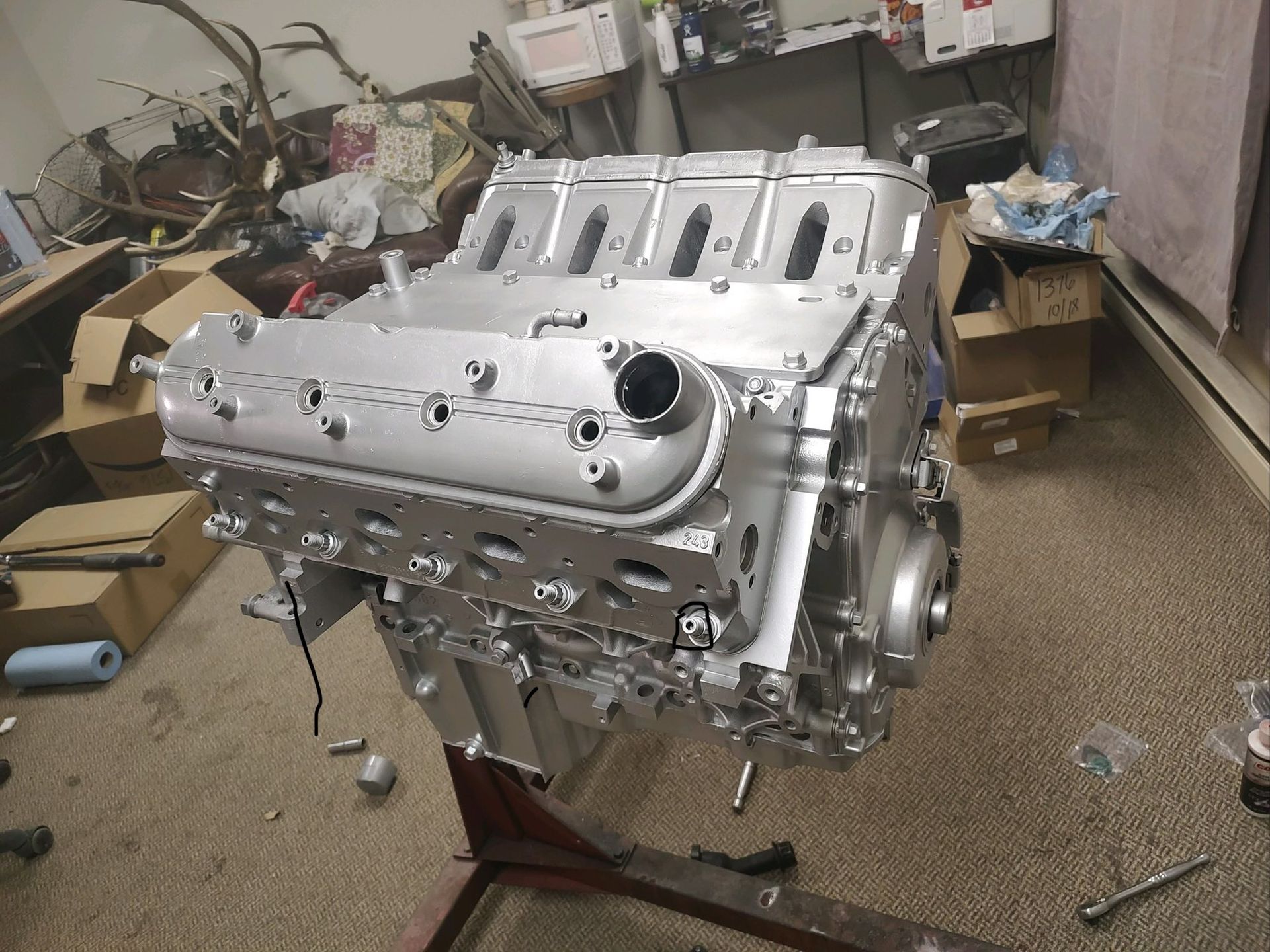 A freshly painted silver V8 engine block mounted on a stand in a cluttered garage.