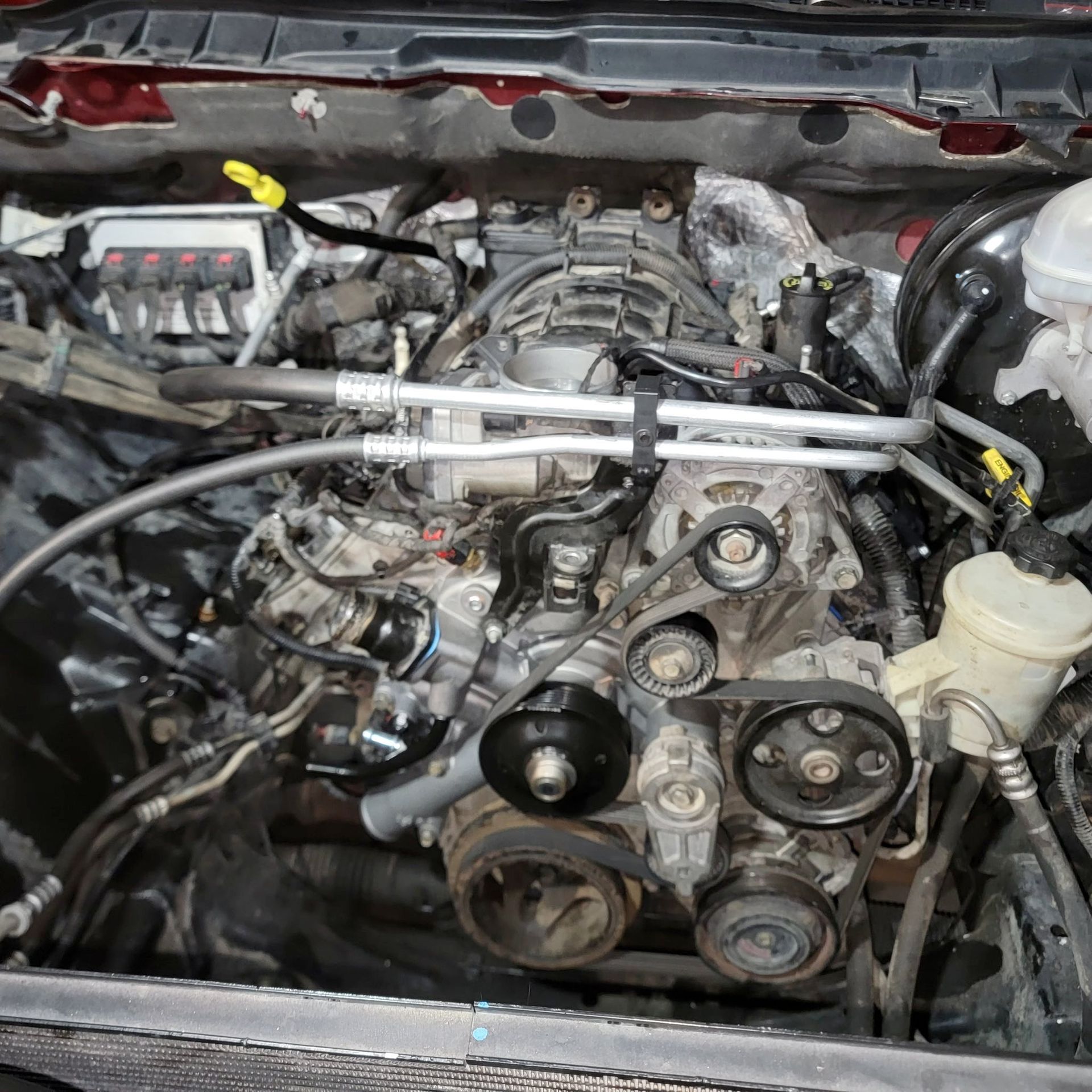 An open hood of a vehicle showing an engine bay with various mechanical components, belts, hoses, and pulleys.