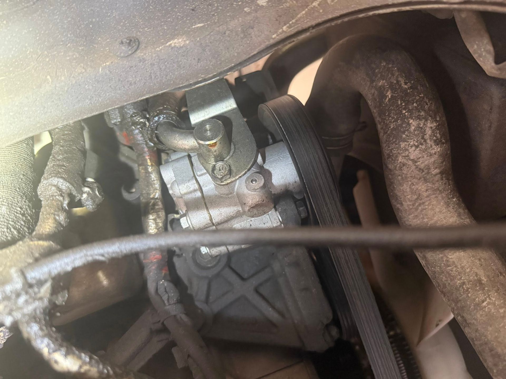 A close-up view of an automotive power steering pump and drive belt inside an engine bay.