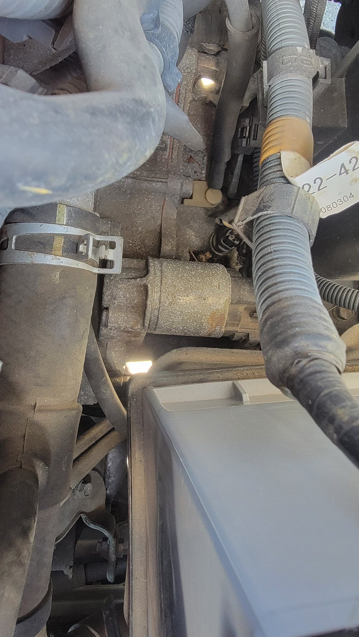 A close-up view of a car engine compartment featuring rubber hoses, a wiring harness with a label, and metal components.