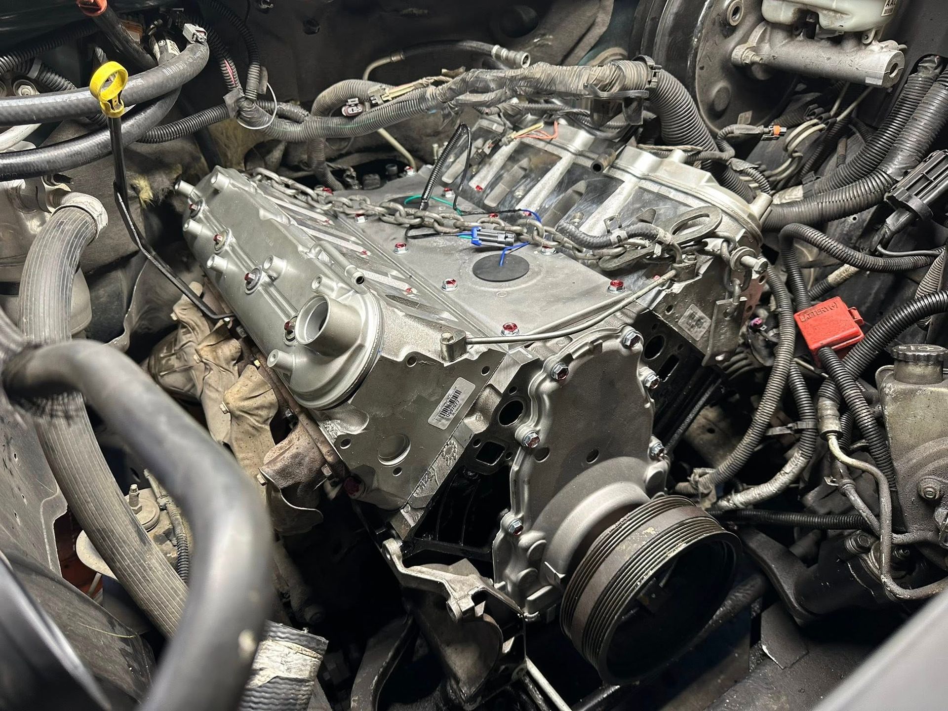 A partially assembled automotive engine inside a vehicle's engine bay, featuring exposed metallic engine blocks and wires.