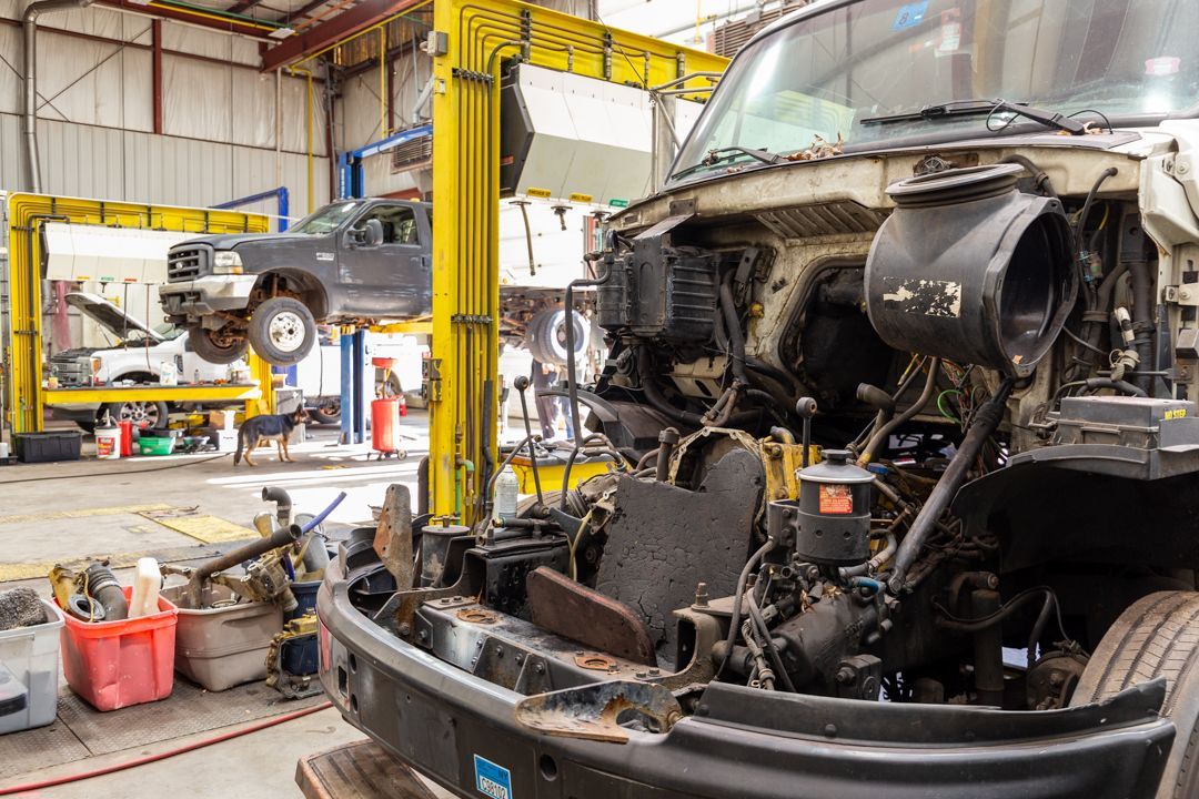 A truck is being repaired in a garage with the hood up.
