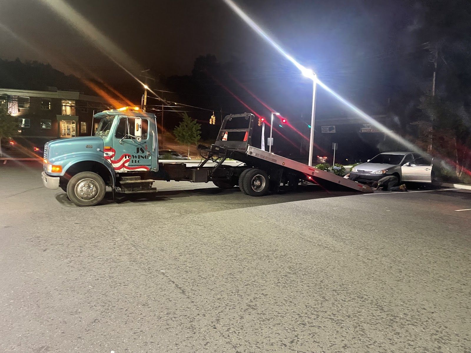 A tow truck is towing a car in a parking lot at night.