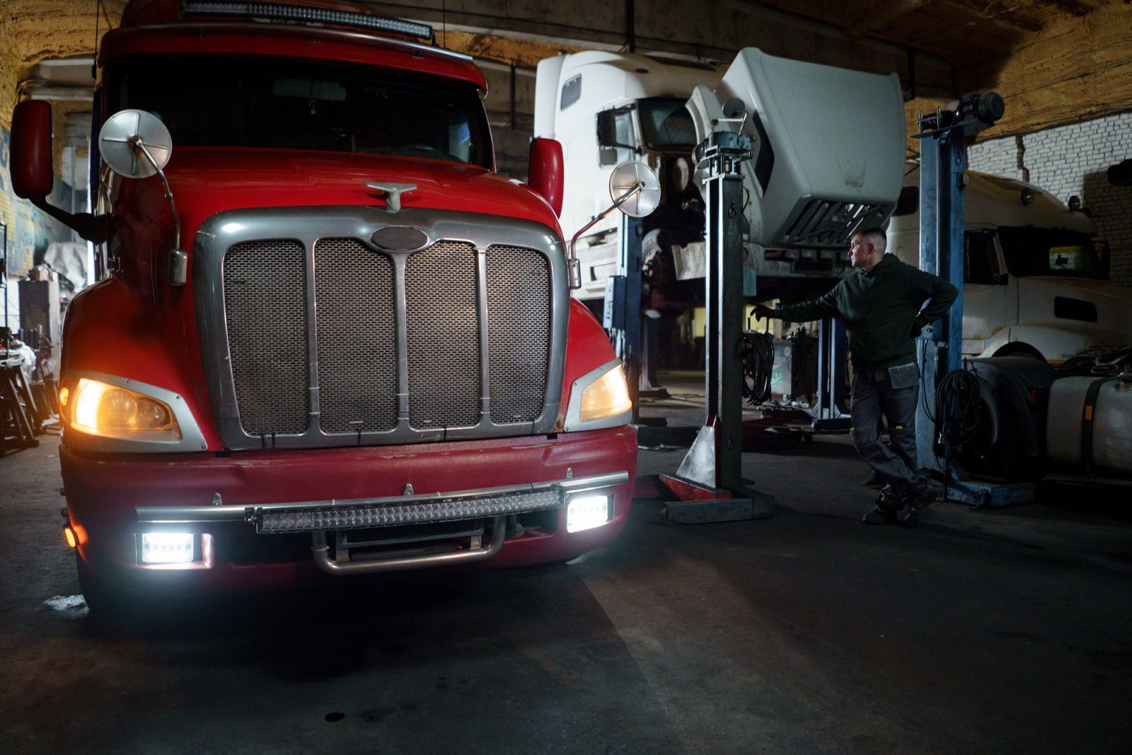 A man is standing in front of a red truck in a garage.