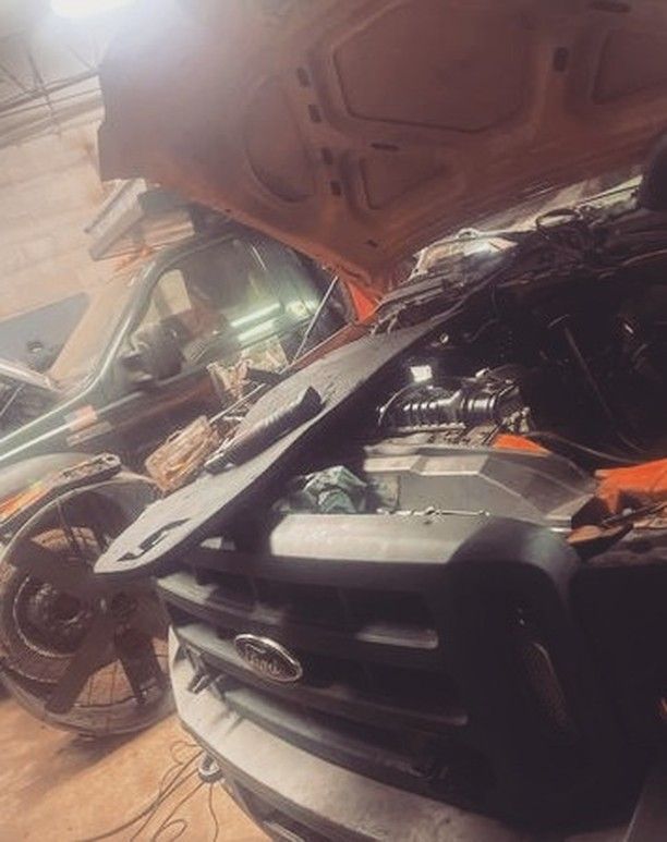 A car with the hood up is being worked on in a garage.