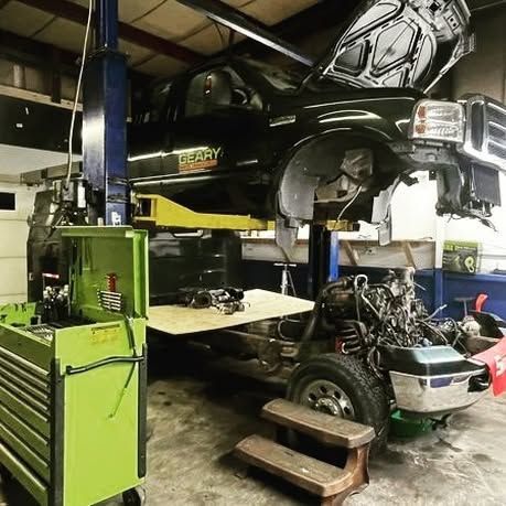 A truck is sitting on a lift in a garage with the hood up.