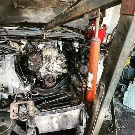 A car engine is being dismantled on a lift in a garage.