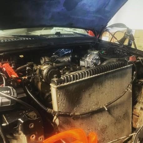 A car with the hood open is being worked on in a garage.