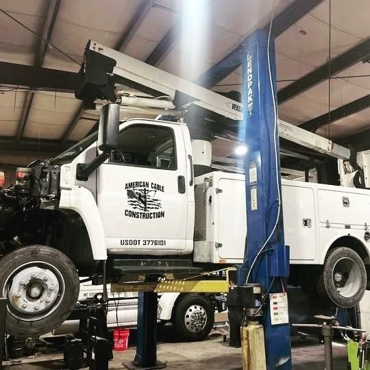 A white construction truck is on a lift in a garage