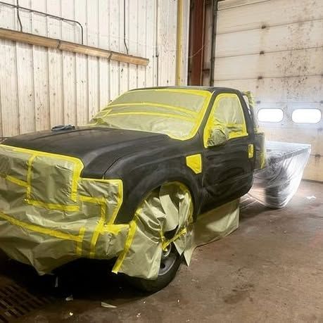 A black truck is covered in yellow tape in a garage.