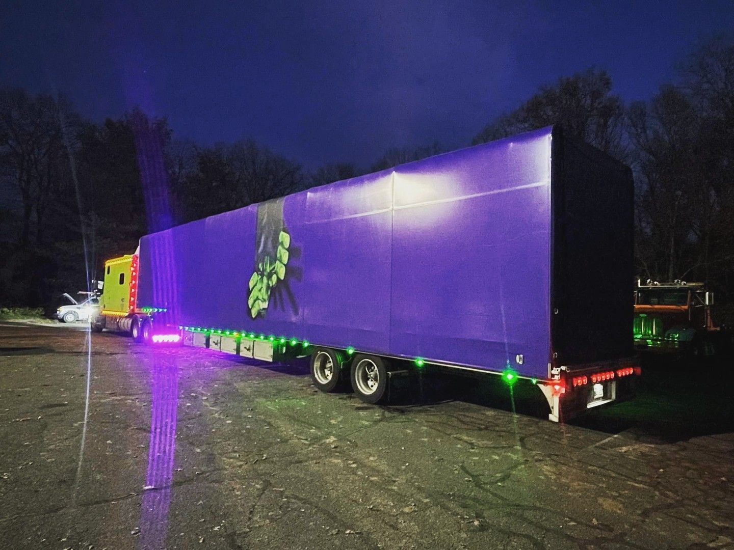 A purple semi truck is parked in a parking lot at night.