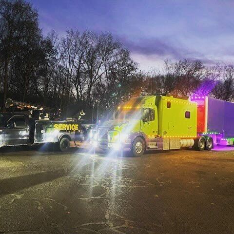 A yellow truck is parked next to a blue truck in a parking lot at night.