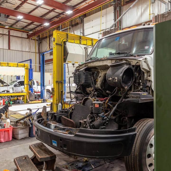 A truck is being worked on in a garage with the hood up.