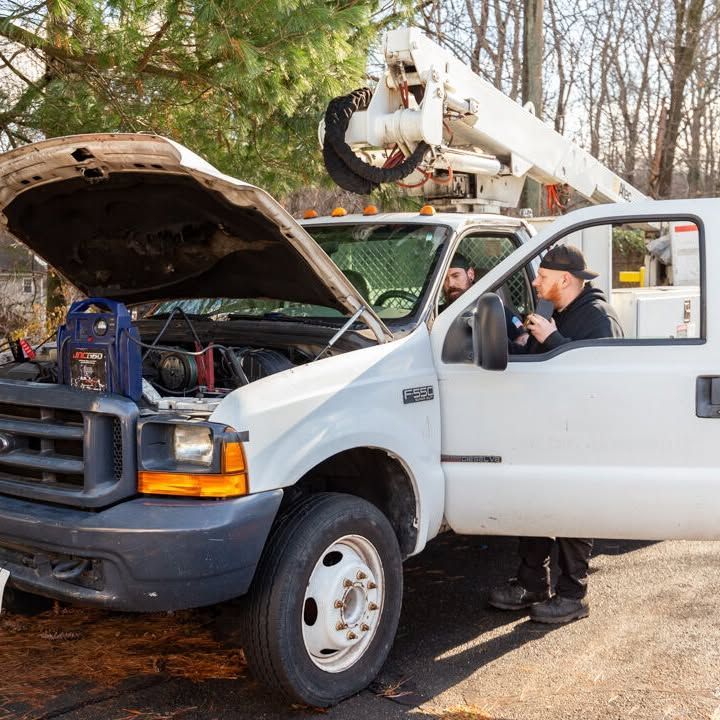A man is standing next to a white truck with the hood open