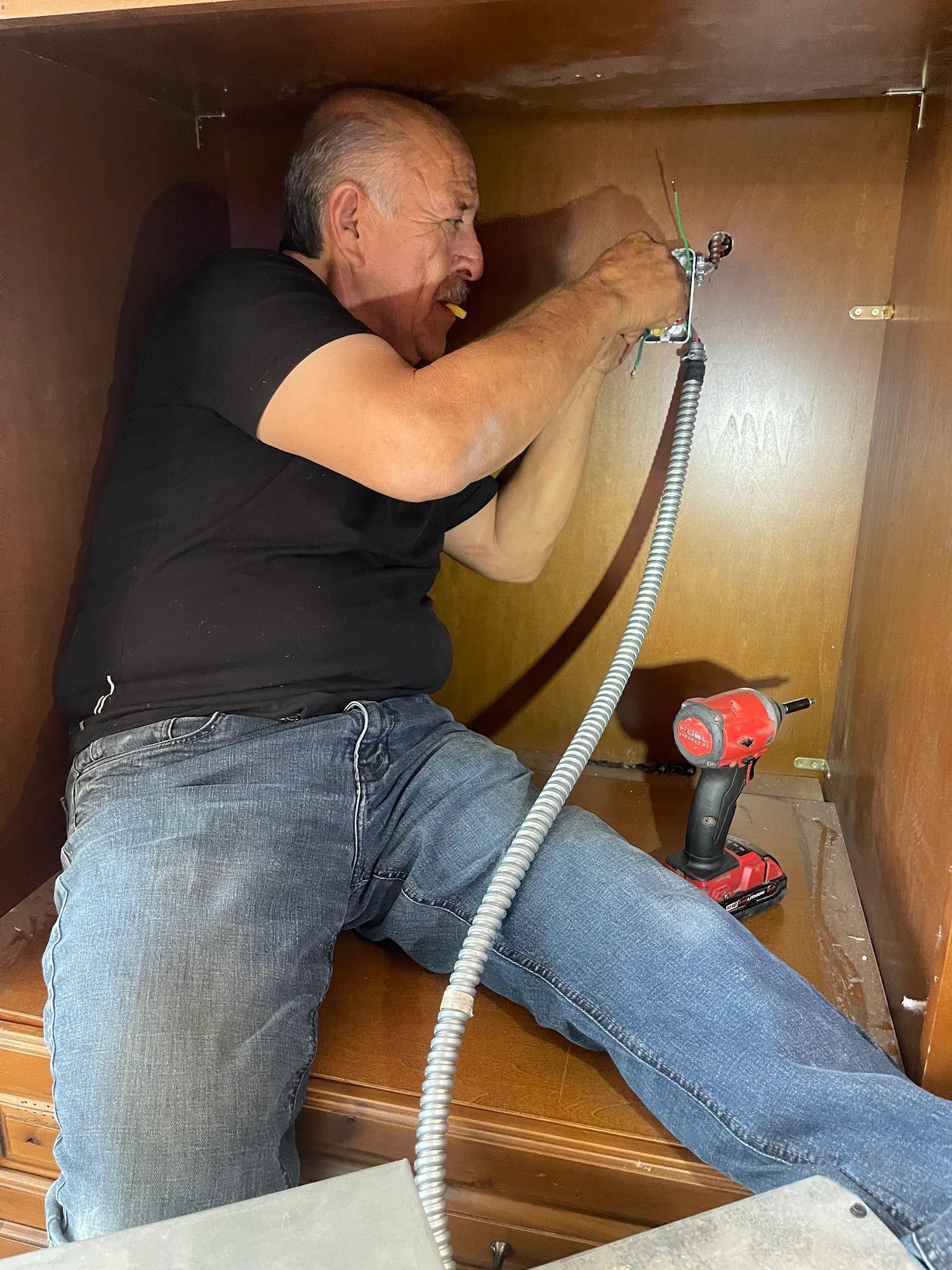 Man in black shirt and jeans, working inside a brown cabinet, using tools.
